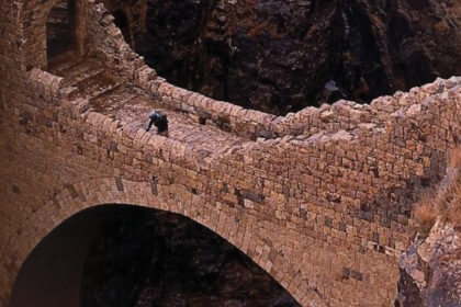 Η πέτρινη γέφυρα Shaharah που ενώνει δύο βουνά πάνω από φαράγγι στην Υεμένη, με θέα την ορεινή φύση και τον ουρανό.