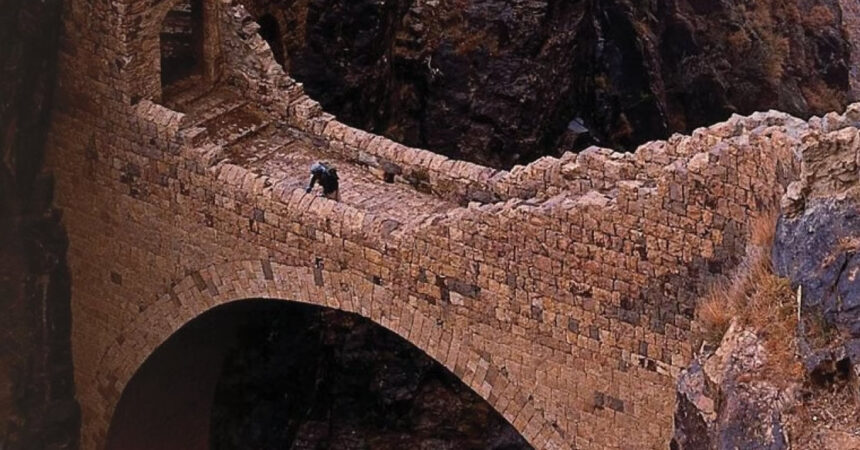 Η πέτρινη γέφυρα Shaharah που ενώνει δύο βουνά πάνω από φαράγγι στην Υεμένη, με θέα την ορεινή φύση και τον ουρανό.