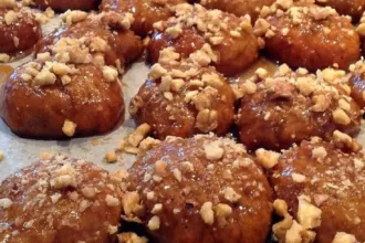 Πυραμίδα από φρεσκοψημένα μελομακάρονα Αγίου Όρους πασπαλισμένα με καρύδι και γυαλιστερά από το μέλι, σε ξύλινη πιατέλα με χριστουγεννιάτικη διακόσμηση στο φόντο