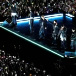 Τα μέλη του συγκροτήματος BTS τραγουδούν σε εξωτερική σκηνή στη Σεούλ μπροστά σε χιλιάδες οπαδούς με φώτα.