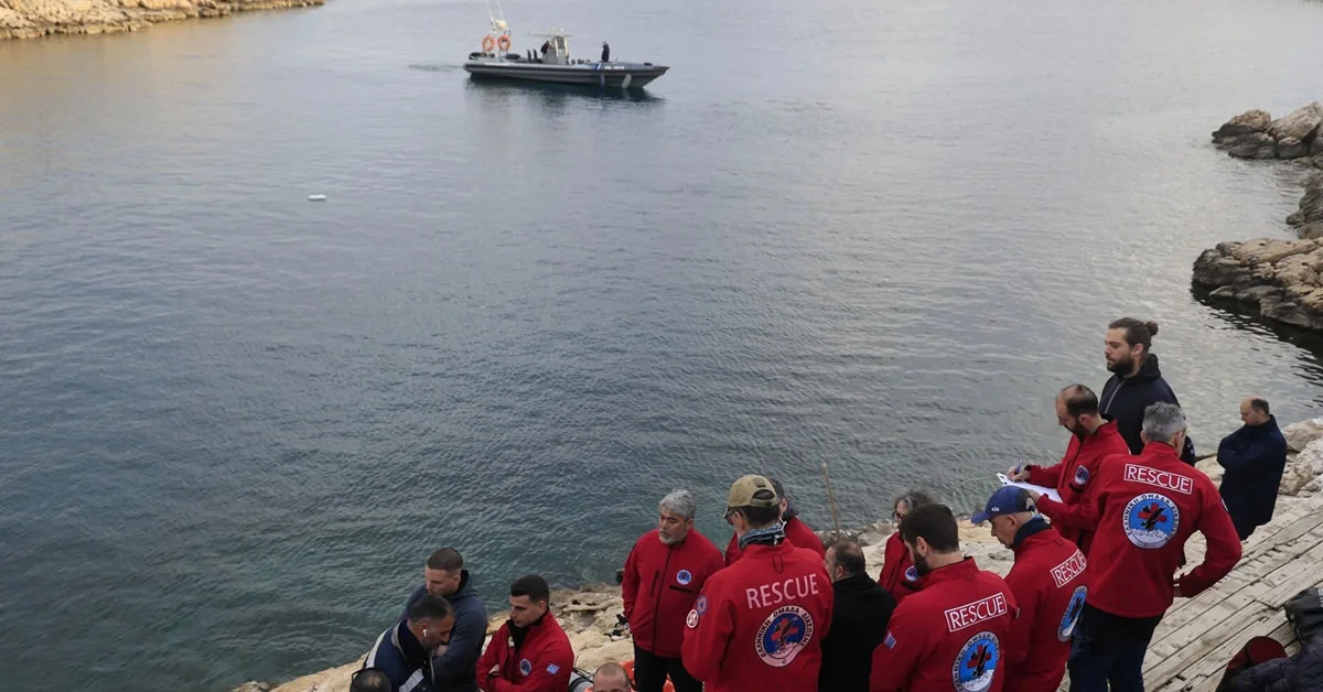 Άνδρες των σωστικών συνεργείων επιχειρούν σε βραχώδη ακτή με φόντο τη θάλασσα, γύρω από σωστικό εξοπλισμό.