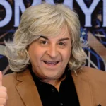 O Μάρκος Σεφερλής με θεατρικό κοστούμι σε σκηνή με έντονο φωτισμό εκτελεί αστείες κινήσεις.
