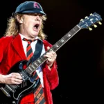 Stevie Young των AC/DC παίζει κιθάρα στη σκηνή φορώντας το χαρακτηριστικό του καπέλο και γιλέκο.