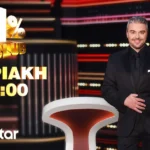 Ο παρουσιαστής Πέτρος Πολυχρονίδης χαμογελαστός στο εντυπωσιακό, φωτισμένο στούντιο του τηλεπαιχνιδιού 1% Club.