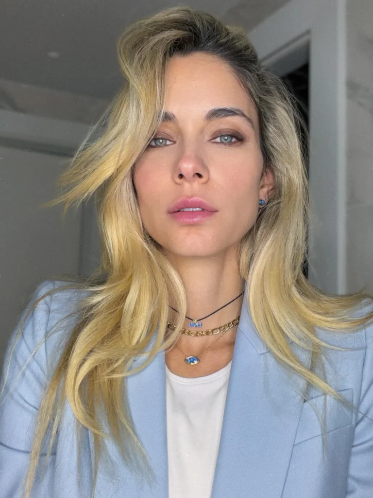Η Δούκισσα Νομικού με γαλάζιο σακάκι, χρυσές αλυσίδες και φυσικό μακιγιάζ.