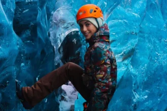 Η Ευγενία Σαμαρά χαμογελαστή με ορειβατικό εξοπλισμό ανάμεσα στους τεράστιους πάγους και τις μπλε παγοσπηλιές του παγετώνα Vatnajökull στην Ισλανδία.