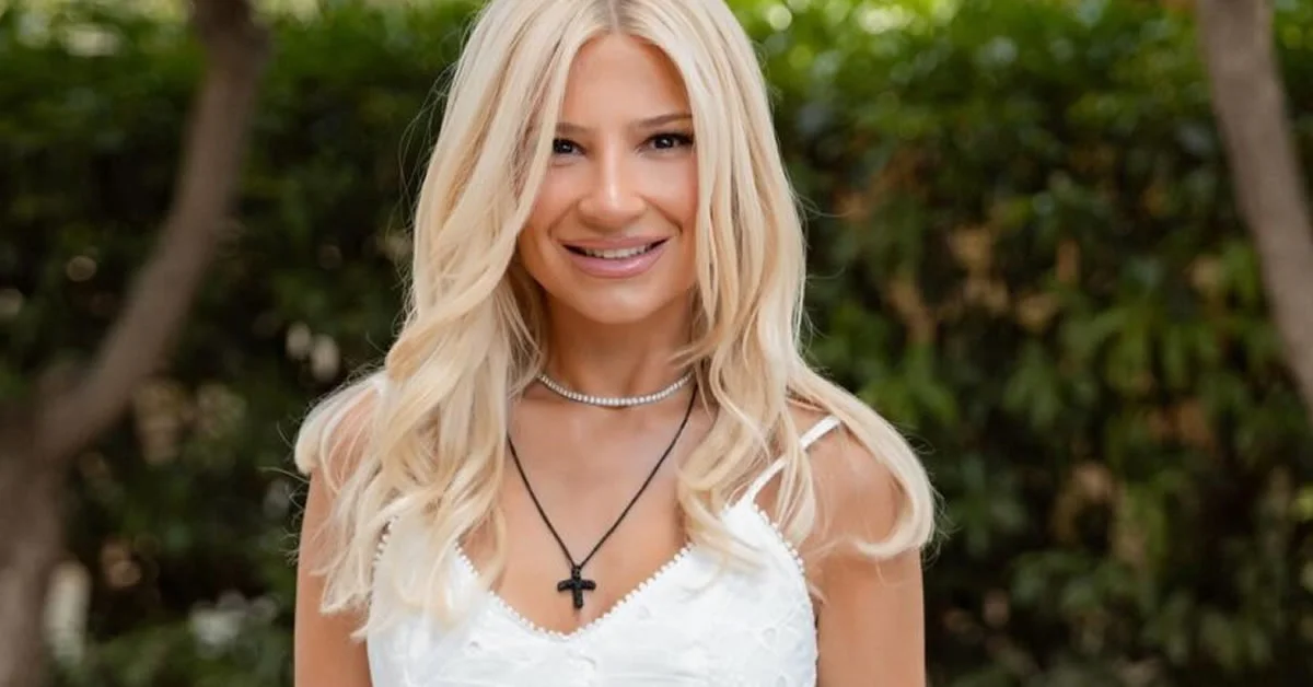 Η Φαίη Σκορδά ποζάρει λαμπερή, φορώντας ένα κομψό λευκό μίνι φόρεμα με λεπτομέρειες δαντέλας και εντυπωσιακά χρυσά ψηλοτάκουνα πέδιλα.